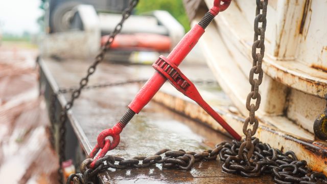 Steel chain and hook securing anchor, using to secure heavy object that transported on the trailer truck. Industrial safety equipment, close-up at the object.